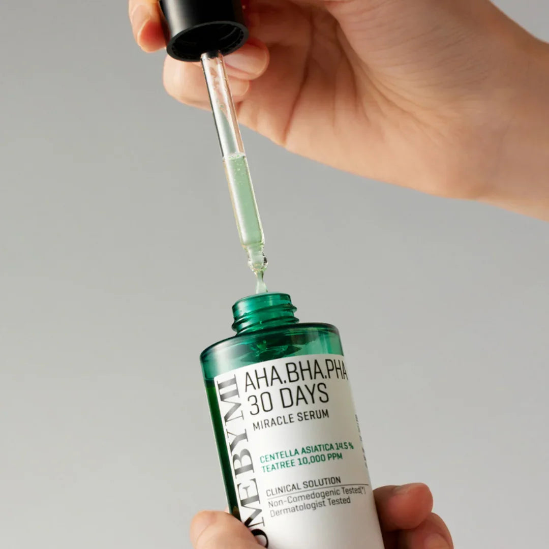 Hand holding a dropper with green serum above a green bottle labeled AHA BHA PHA 30 Days Miracle Serum skincare product