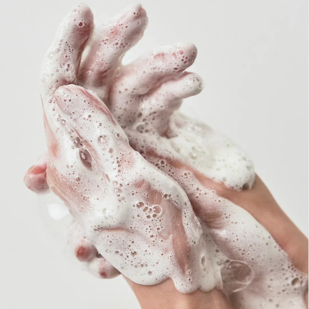 Hands covered in rich foam cleansing suds against a plain white background