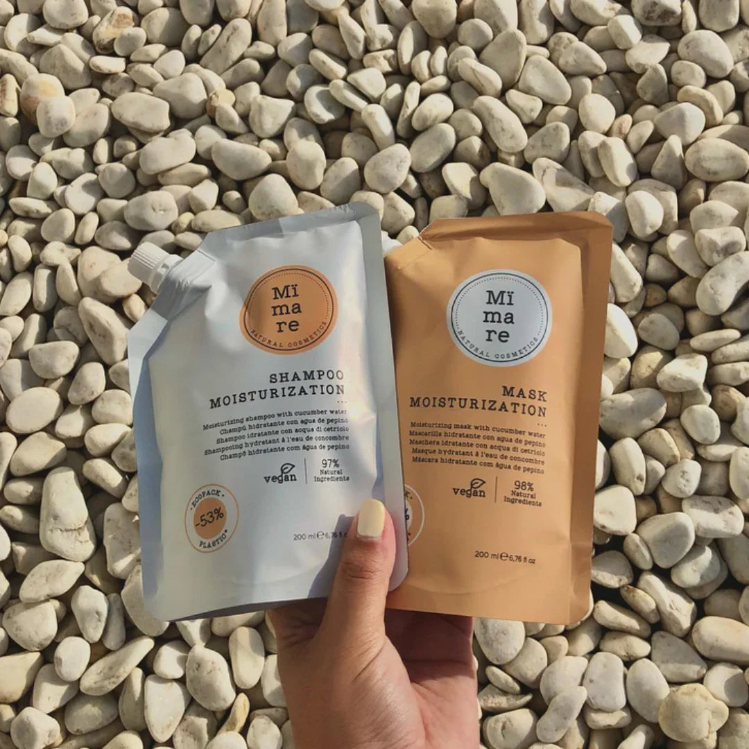 Hand holding Mimare Moisturization Shampoo and Mask pouches on white pebbles, vegan and natural ingredients