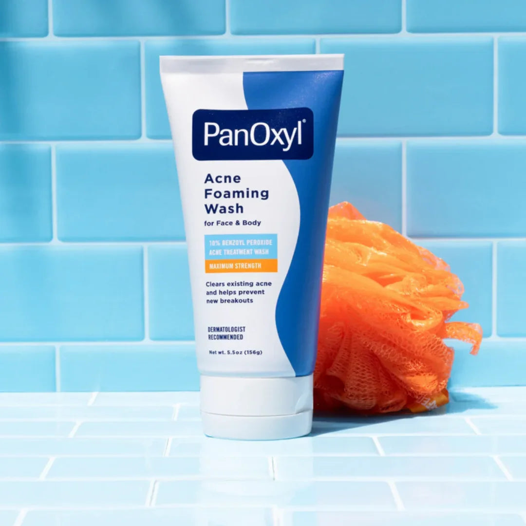 PanOxyl Acne Foaming Wash tube with benzoyl peroxide, next to an orange bath sponge on blue tiled background