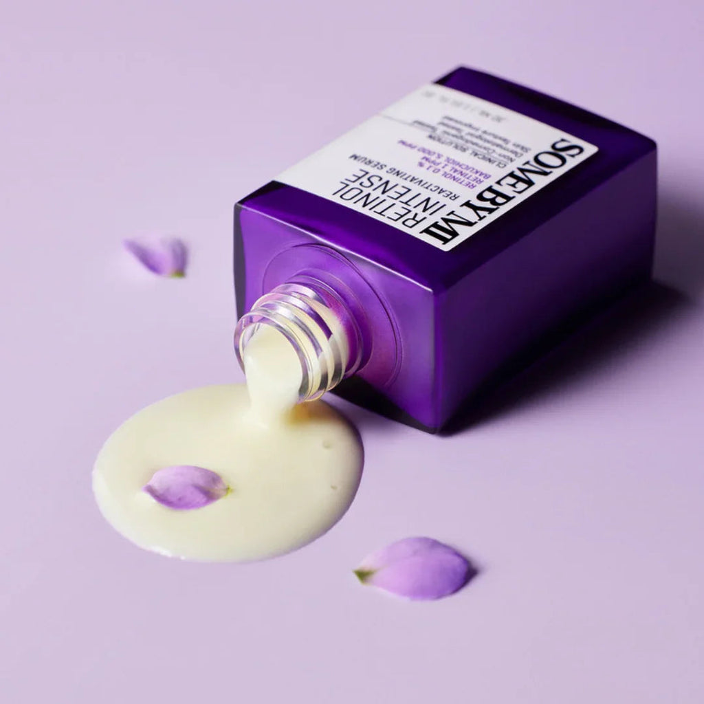 Purple bottle of SOMEBYMI Retinol Intense Reactivating Serum spilling cream on lavender surface with purple flower petals