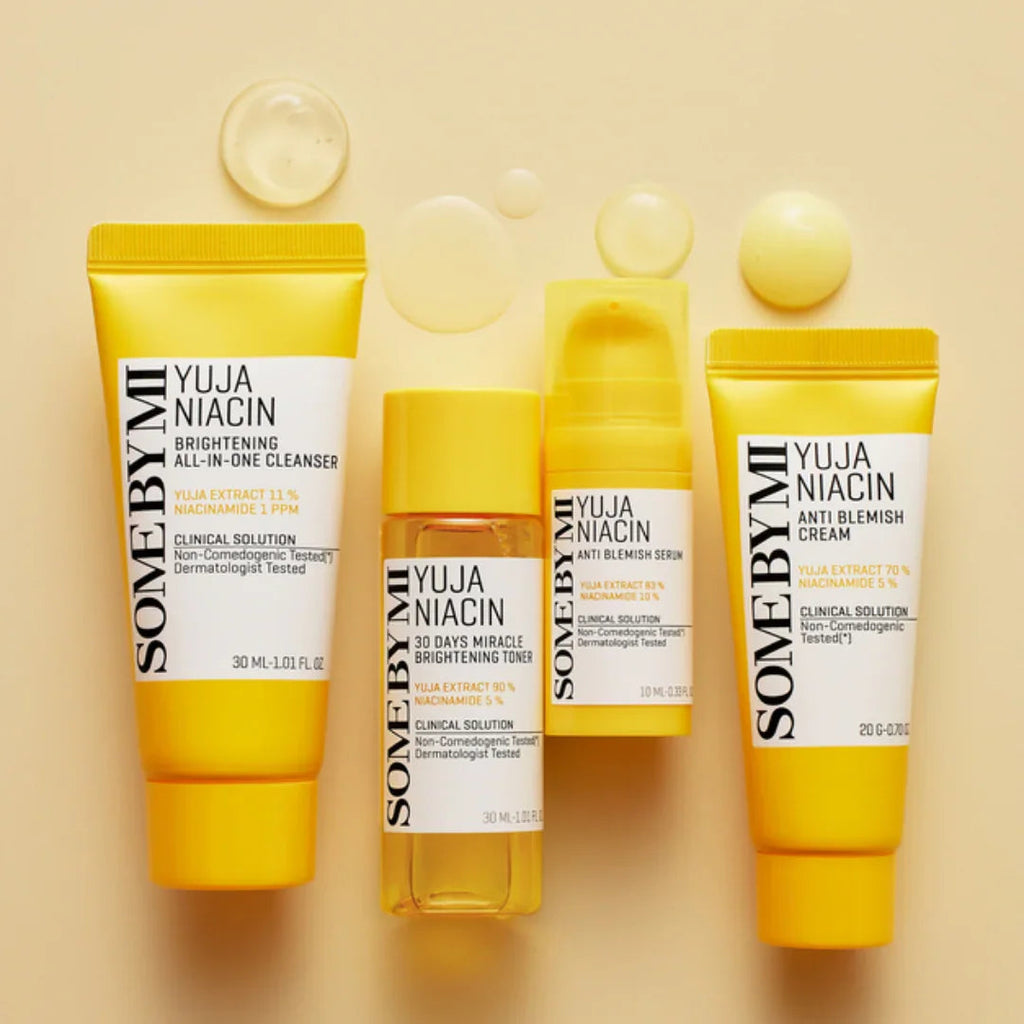 Some By Mi Yuja Niacin brightening cleanser, toner, anti-blemish serum, and cream in yellow packaging on beige background